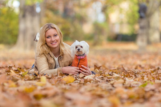 Beautiful young woman playing with her dog in autumn leaves