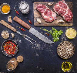 Fresh raw pork steak on a cutting board with a knife and fork for the meat with hot red peppers, lemon and butter on wooden rustic background top view place for text,frame