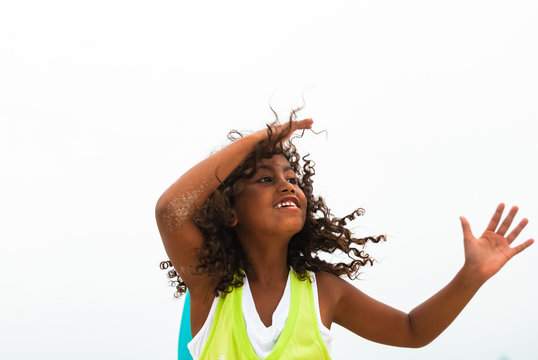 Beautiful brazilian girl posing outdoor on a cloudy summer day. Happy female child with long curled hair, wearing white and green t-shirt against white background