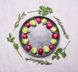 raw Brussels sprouts and radishes with herbs in a frying pan on wooden rustic background top view close up place for text,frame