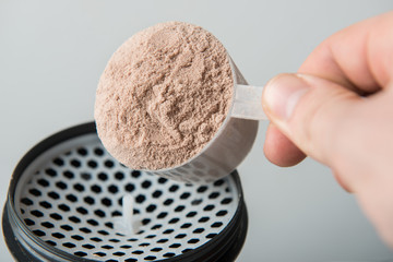 Scope of chocolate whey isolate protein next to the translucent protein shaker, with focus on the protein inside the scoop.