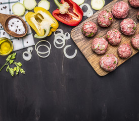 meat balls with herbs and onions on a cutting board with vegetables, spices, oil, vintage wooden spoon on wooden rustic background top view border ,place for text