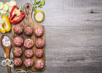 Ingredients for cooking meat balls with herbs and onions on a cutting board with tomatoes, peppers, zucchini and herbs on wooden rustic background top view border ,place for text 