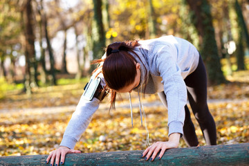 Attractive sporty woman with headphones doing push ups outdoors in the park