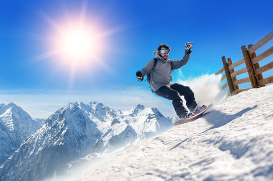 Snowboarder freerider / Snowboarder man holding snowboard in the air jumping with mountains on background