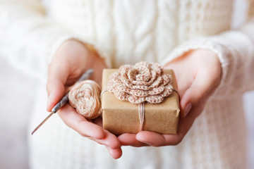 Woman in white knitted sweater holding a present and coil of thread and crocheting hook. DIY present. © Konstantin Aksenov
