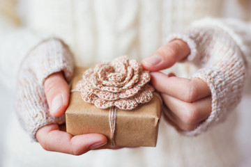 Woman in white knitted sweater and mitts holding a present. Gift packed in craft paper with...