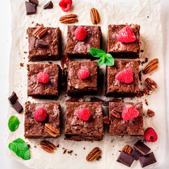  Brownie pieces with nuts decorated with berries and mint leaves on the white paper.