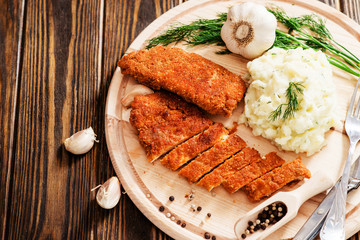 
meat with garnish , chicken cutlets in breadcrumbs , boiled mashed potatoes with herbs , garlic and spices on a wooden background