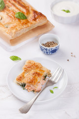 Traditional pie with salmon, spinach and basil on a white table