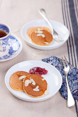 Pumpkin pancakes with honey, nuts and jam in a white plate on a table.