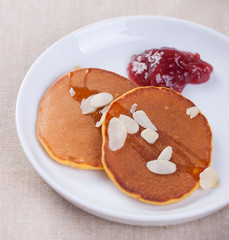 Pumpkin pancakes with honey, nuts and jam in a white plate on a table. Closeup.