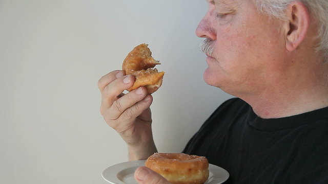 profile view of older man eating a fresh doughnut