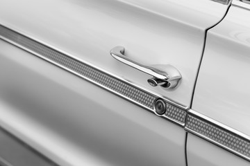 Close-up of car door handle of a white shiny classic vintage car