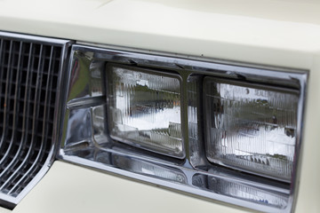 Close-up of rectangle shape headlights of a white shiny classic vintage car