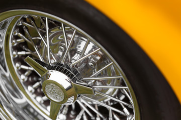 Close-up of spoke wheel of a yellow shiny classic vintage car