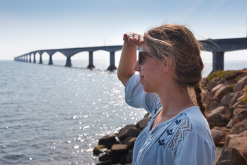 Woman looking at sea with Confederation Bridge in the background, Prince Edward Island, Canada
