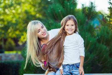 Fototapeta premium Woman brushing her daughter hair outdoors jeans