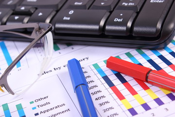 Obraz premium Pen, glasses and computer keyboard on financial graph, business concept