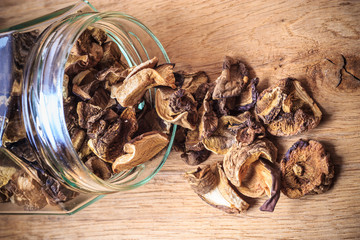 Dry mushrooms in jar on wooden table.