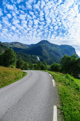 Narrow curvy road with scenic background of mountains and clouds