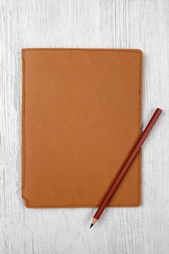 brown notebook and a pencil on white wooden table, top view