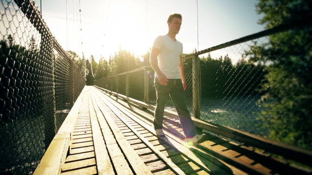 Motion-Photo (Cinemagraph) of a Young Man Crossing a Solid Hanging Bridge over a Flowing Water River