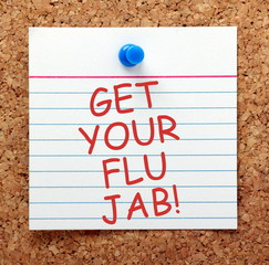 The words Get Your Flu Jab in red text on a note card pinned to a cork notice board as a reminder