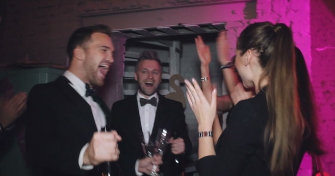 Excited men walking downstairs and bringing champagne to their ecstatic friends in night club 
