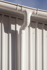 New white rain gutter on a building with white metal sheet against blue sky