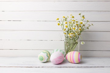 Bouquet of chamomiles in a glass vase and easter eggs in pastel