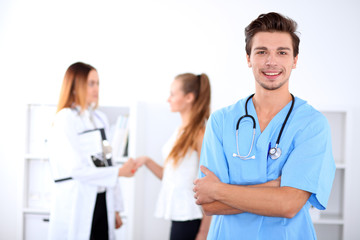 Attractive male doctor in front of medical group, crossed arms