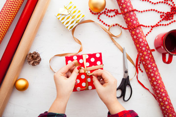 Female hands wrapping xmas gifts into paper and tying them up wi