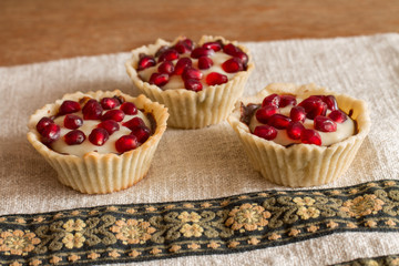 Three tartletes with custard and pomegranate on linen tablecloth with pattern pattern. 