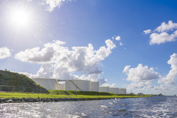 Storage tanks placed along the shore. Cloudy and smokey sky at the background. Typical industry background.