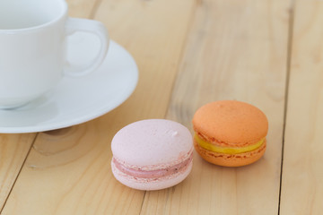 Macaroons with cup on wooden background.