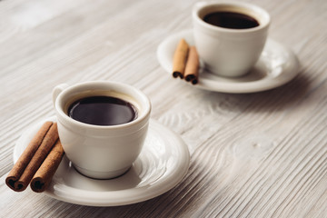Cups of coffee with cinnamon sticks on a white wooden background