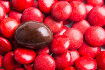 Concept of selective focus on brown chocolate candy against heaps of red candies at background