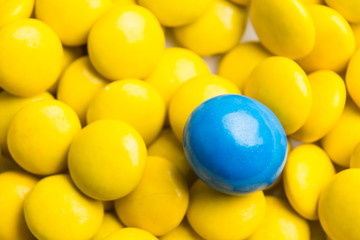 Concept of selective focus on blue chocolate candy against heaps of yellow candies at background