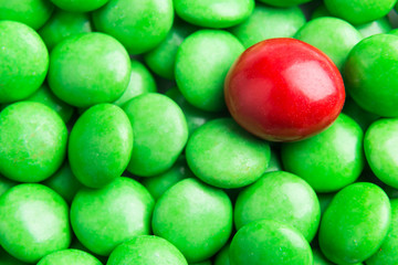 Concept of selective focus on red chocolate candy against heaps of green candies at background