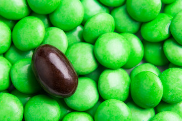 Concept of selective focus on brown chocolate candy against heaps of green candies at background