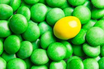 Concept of selective focus on yellow chocolate candy against heaps of green candies at background