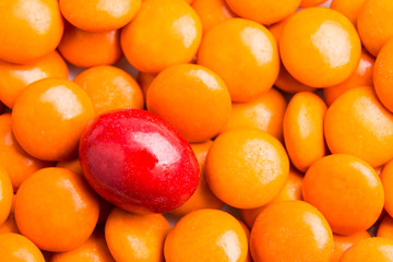 Concept of selective focus on red chocolate candy against heaps of orange candies at background