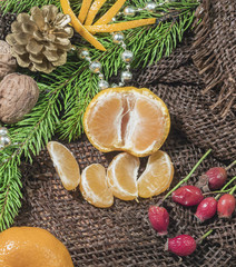 Obraz na płótnie Canvas on a table covered with burlap are candles are tangerines, cones, fir or pine twig and berries. Christmas design