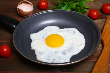 Pan of fried eggs, with cherry-tomatoes and parsley on a wooden table surface