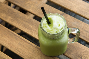 Delicious of green tea frappe with tube in glass cup on wood table. homemade.