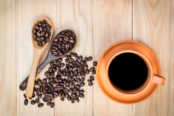 Coffee in ceramic cup and roasted coffee beans on wooden table. Top view. Pottery coffee cup. (Selective focus on cup)