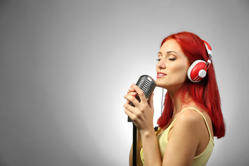 Beautiful young woman with microphone and headphones on gray background