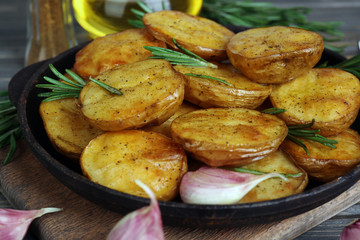 Delicious baked potato with rosemary in frying pan on table close up