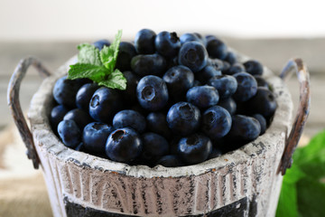 Tasty ripe blueberries with green leaves in bucket on table close up